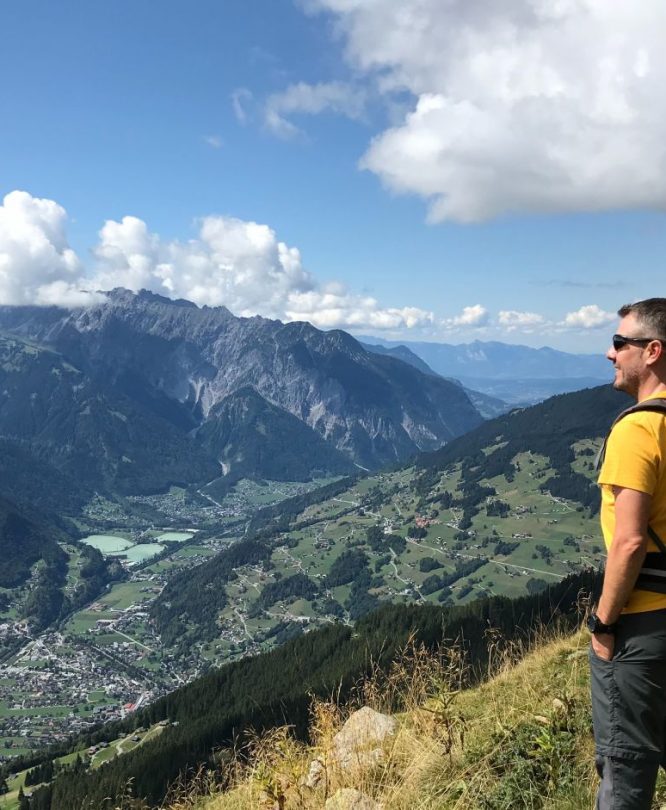 Ein Wanderer blickt vom Gipfel aus zufrieden ins Tal (Montafon, Schruns)