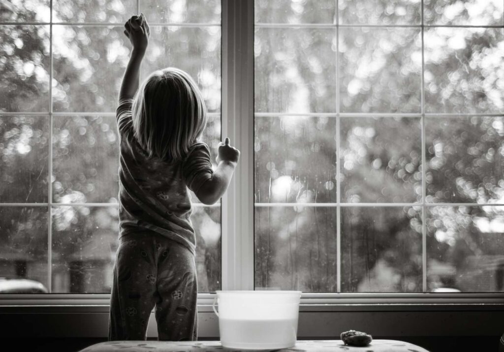 Schwarzweiß-Bild: Kind putzt Fenster mit Schwamm und Wasser